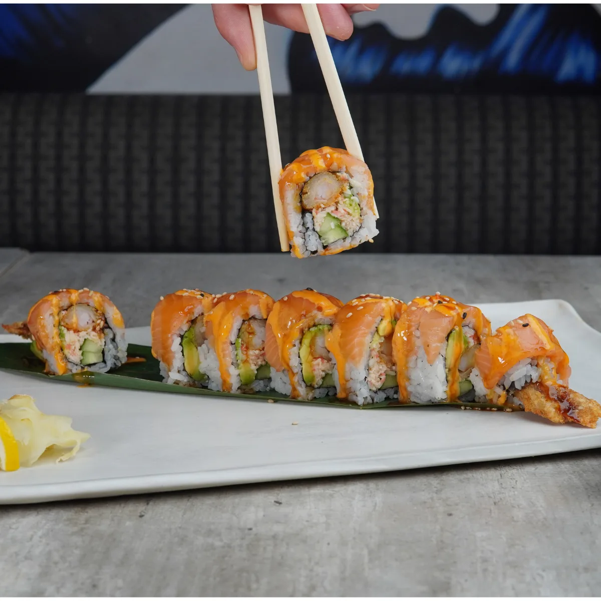 A Red Dragon roll of jumbo shrimp, avocado, crab mix and cucumber under slices of fresh salmon, one piece lifted on chopsticks
