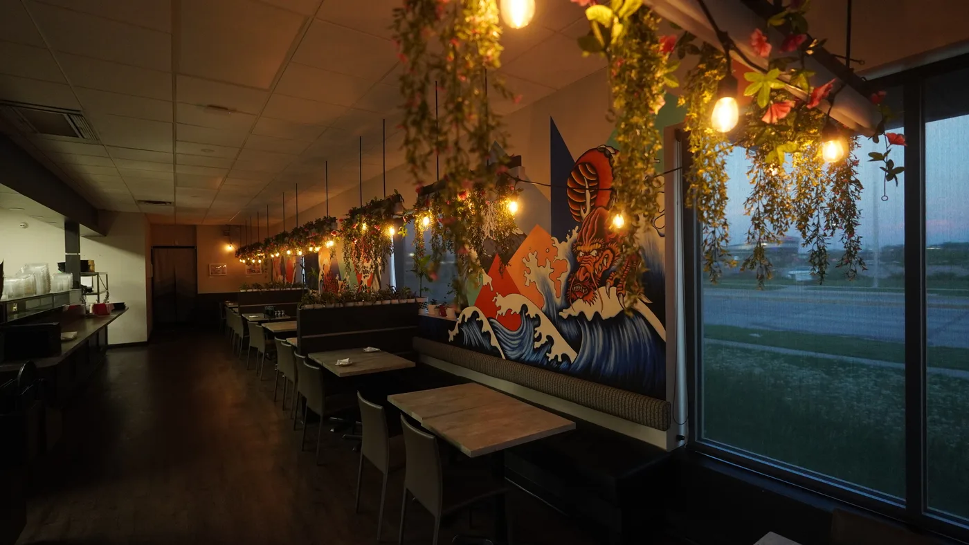 The long dining room at dusk, with booths along the mural wall and lights strung overhead