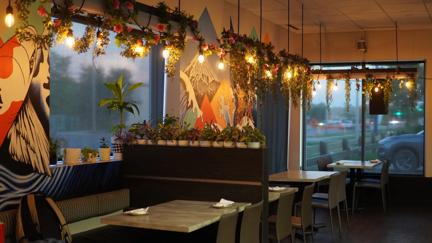 The dining room by day: wooden tables, potted plants and string lights in front of a painted wave mural